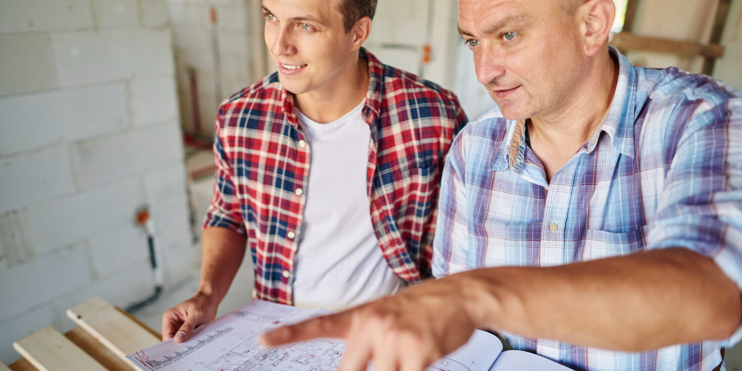 handsome-young-carpenter-working-with-experienced-man Contractor discussing home renovation plans to avoid common remodeling mistakes